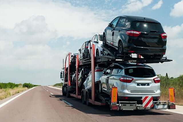 car transport showing an open car trailer driving down a narrow highway on a partially cloudy day