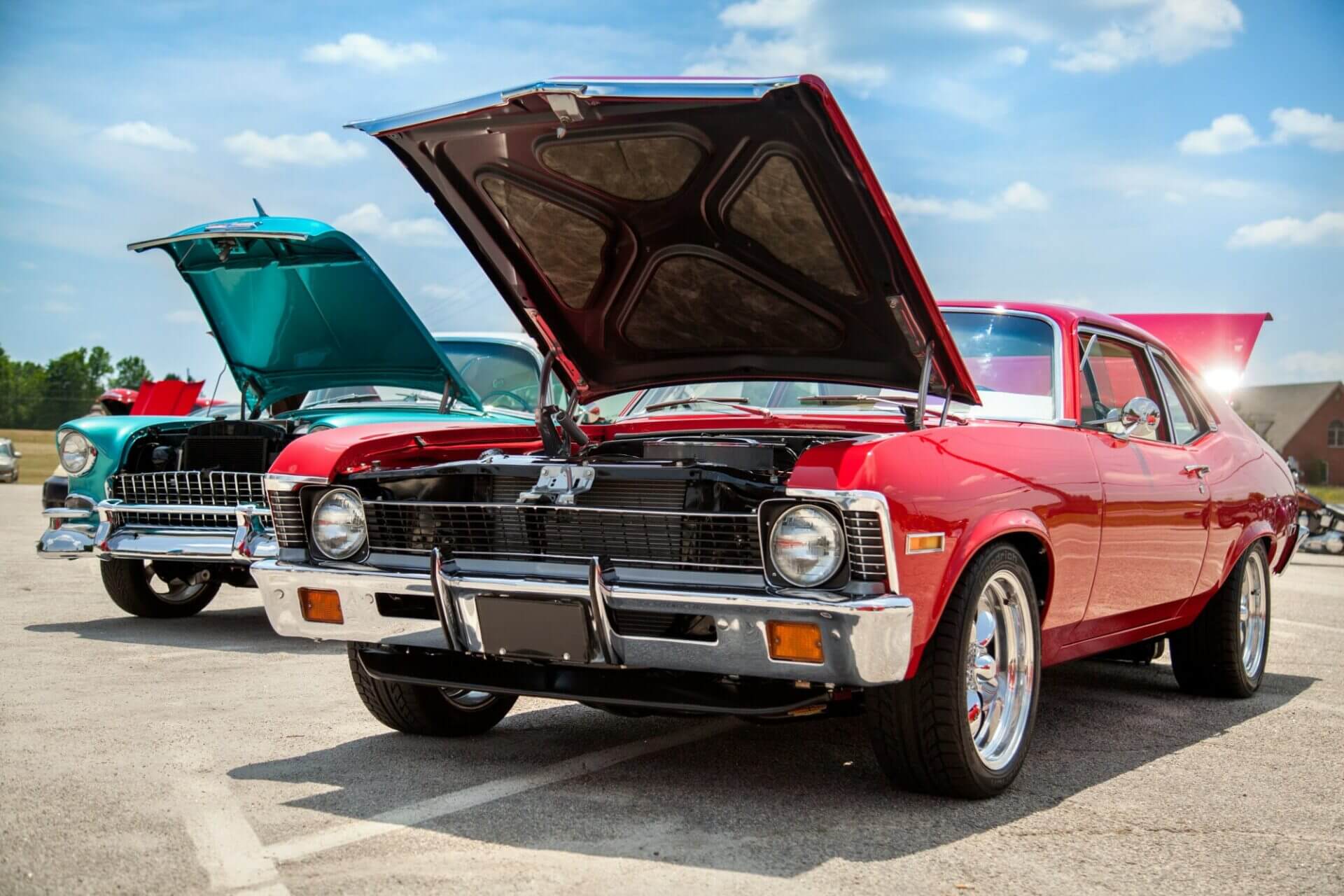 classic cars for sale Two American muscle cars with hoods open in parking lot on a sunny day. American dream cars des moines. You might be asking where can I buy classic cars. Read this blog post to find old school cars for sale.