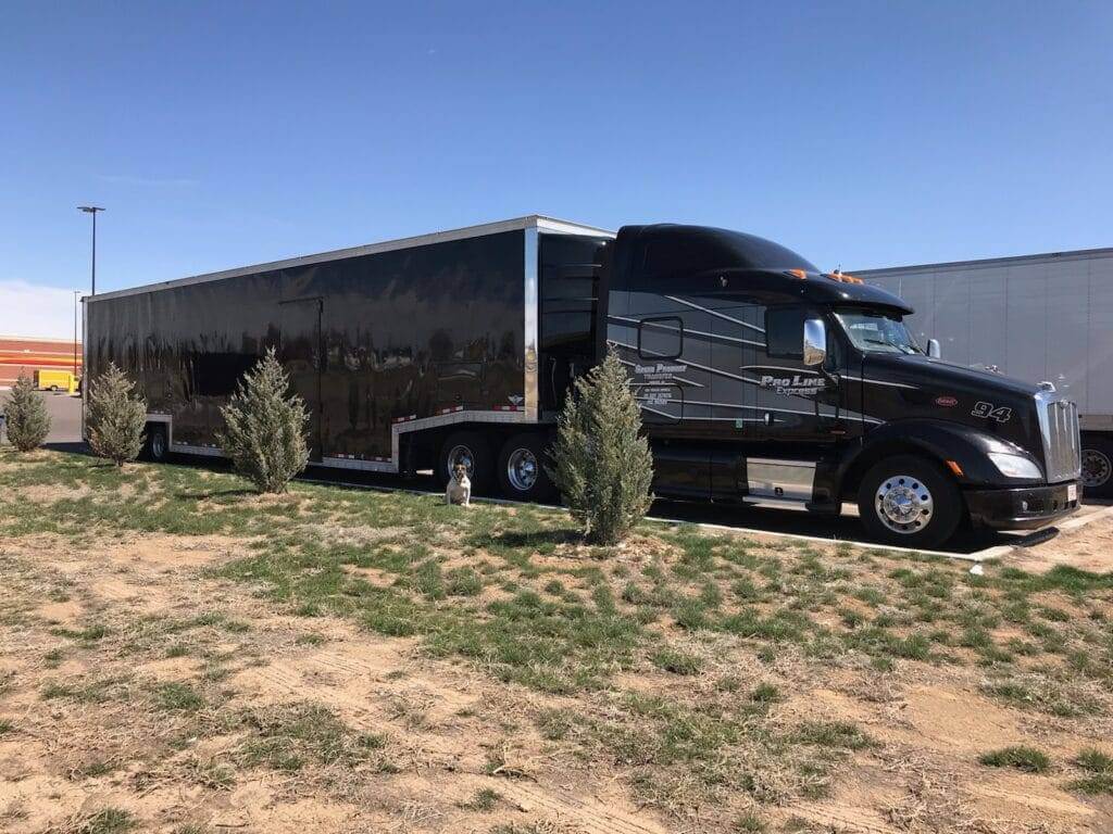 auto transport Black semi truck with black enclosed car trailer in a parking lot on a sunny day