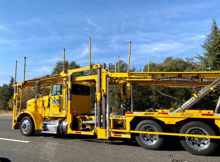 auto transport yellow semi truck with an empty yellow open car trailer driving from right to left on a right sunny day