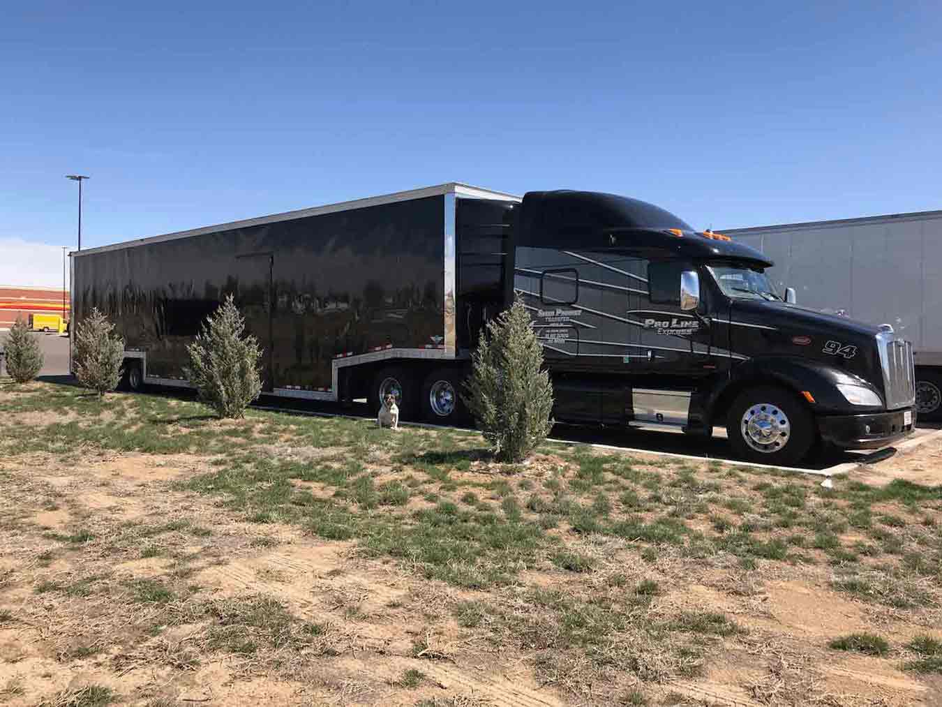 Black Semi Truck with Black Enclosed Car Trailer in a Parking Lot on a Sunny Day | National Transport Services