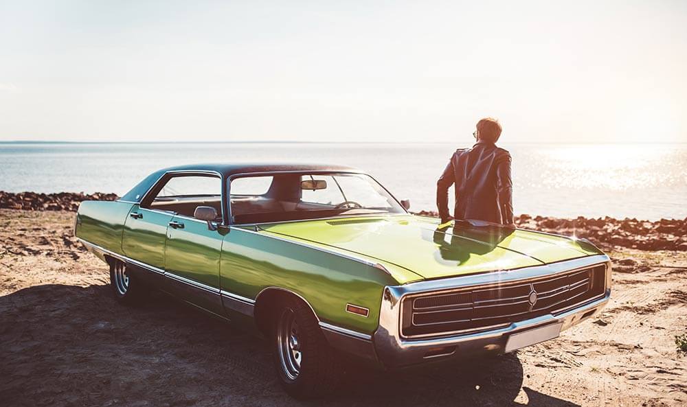 Man leaning against a classic car at the beach.