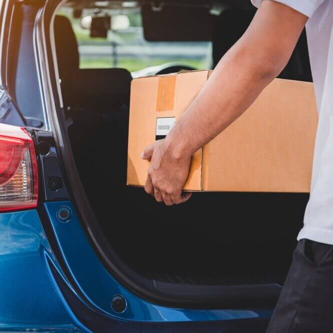 A man puts a cardboard box in his trunk. Shipping a car with personal items.