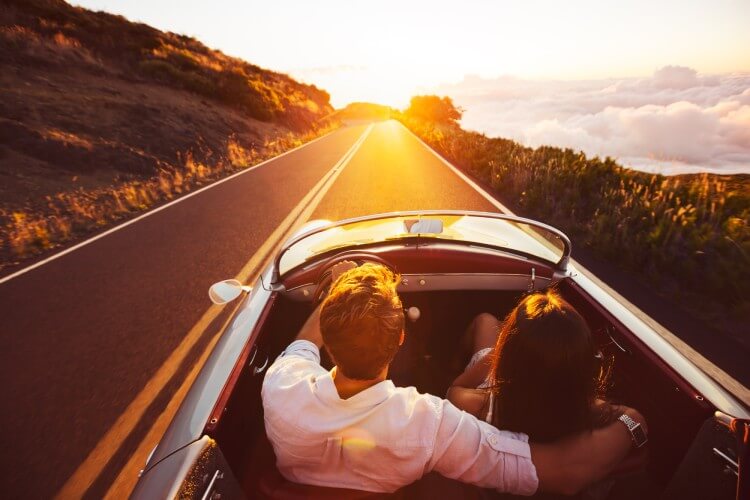 A couple drives in a classic convertible at sunset.