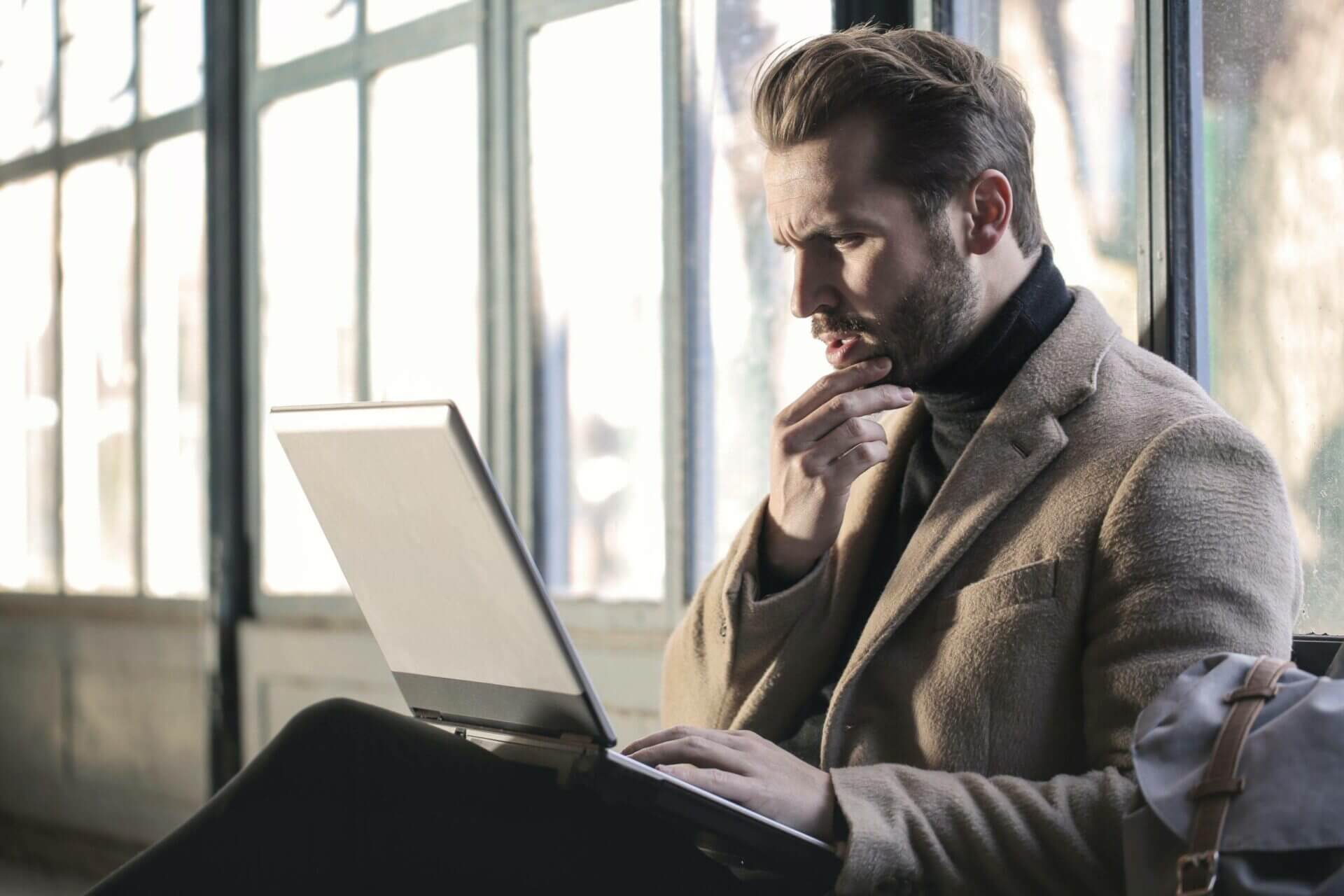 A man sitting wearing an overcoat looking at his laptop. How Much is it to Ship a Car?