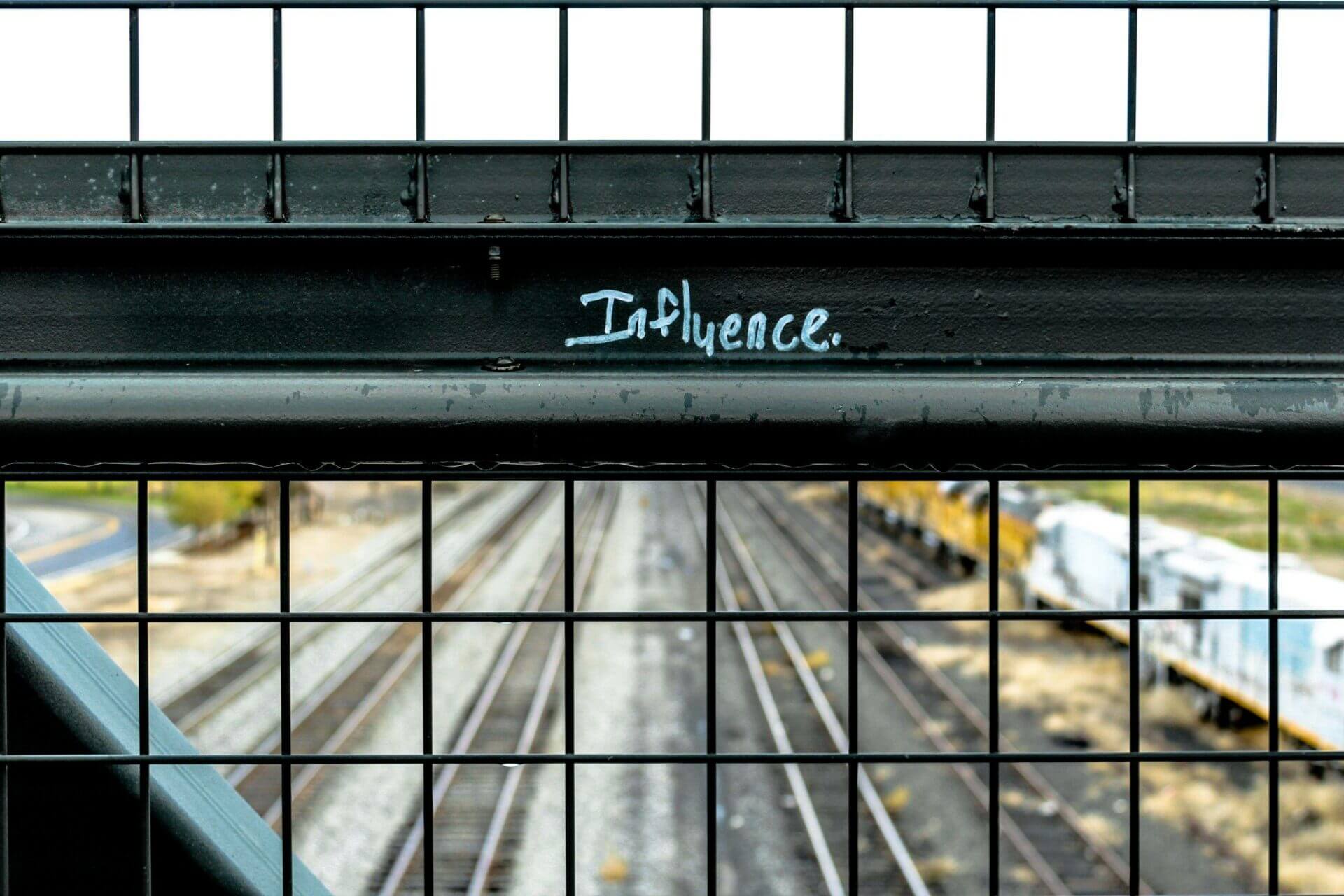 The word "Influence" is written on a fenced overpass of a railway. Shipping costs for cars.
