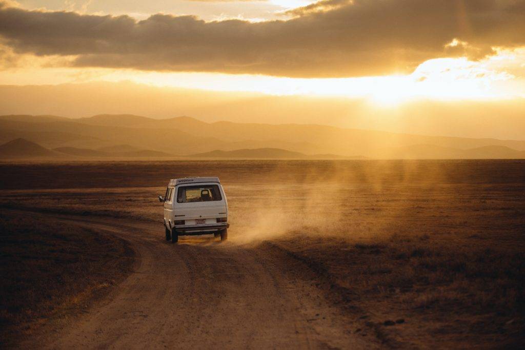 A white minivan on an empty desert road. Why People Choose Auto Transport Services