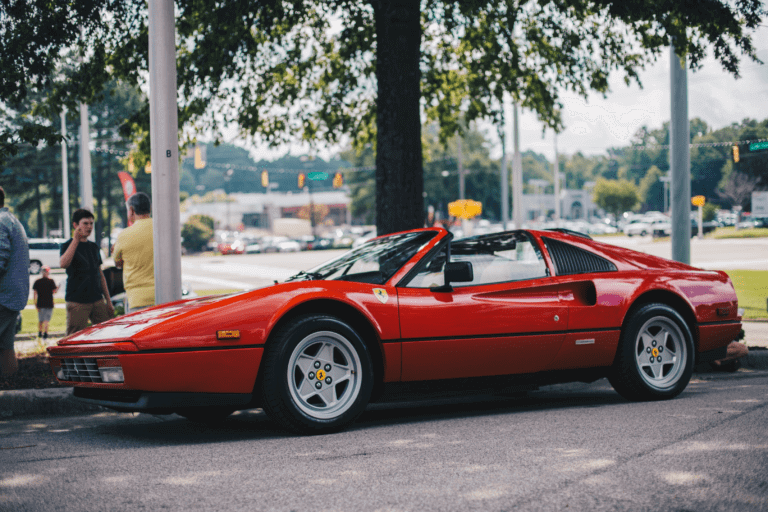 A classic red Ferrari 328 GTS is parked in front of a park. We ship classic car and luxury vehicle.