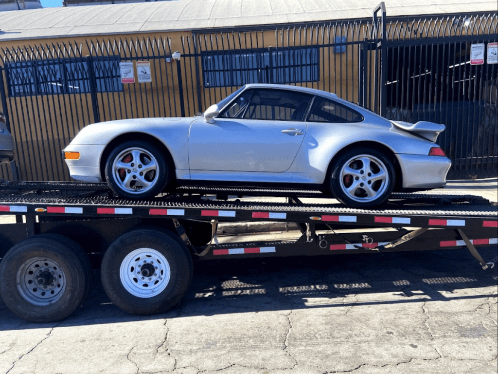 A silver 1996 Porsche 993 Turbo loaded on a open wedge 3 car trailer