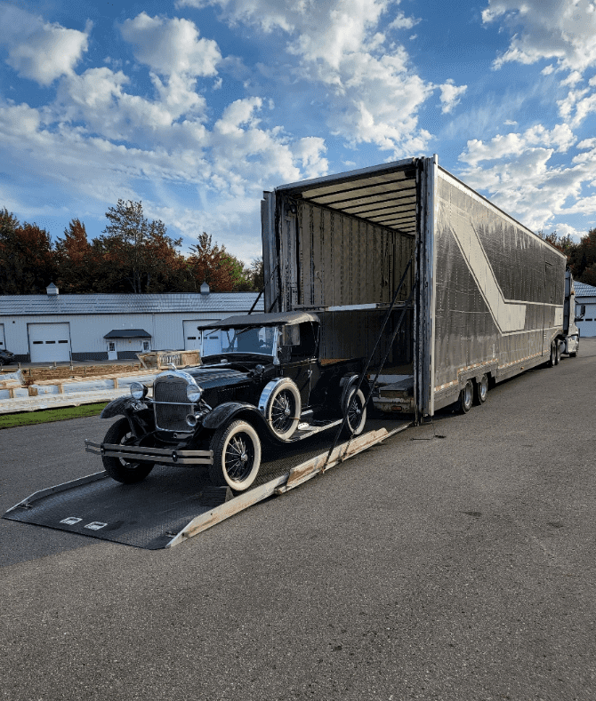 A vintage Ford pickup on a liftgate, getting loaded into an enclosed auto transport truck.