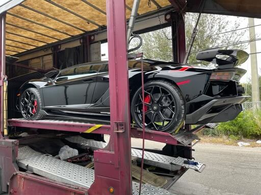 A black Lamborghini Aventador loaded on a closed transport trailer. An enclosed car hauler is how all exotic cars are transported. Enclosed auto shipping is the safest, most secure way to ship a car.