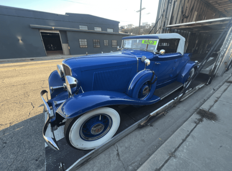 A blue 1930s classic convertible car getting loaded on a hydraulic lift gates.