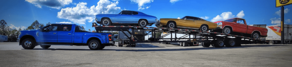 A blue Ford dually pickup truck hauling a three-car wedge trailer that has three classic cars on it. If you want to ship a car by an enclosed auto transport trailer, we can provide you with a ca shipping quote.