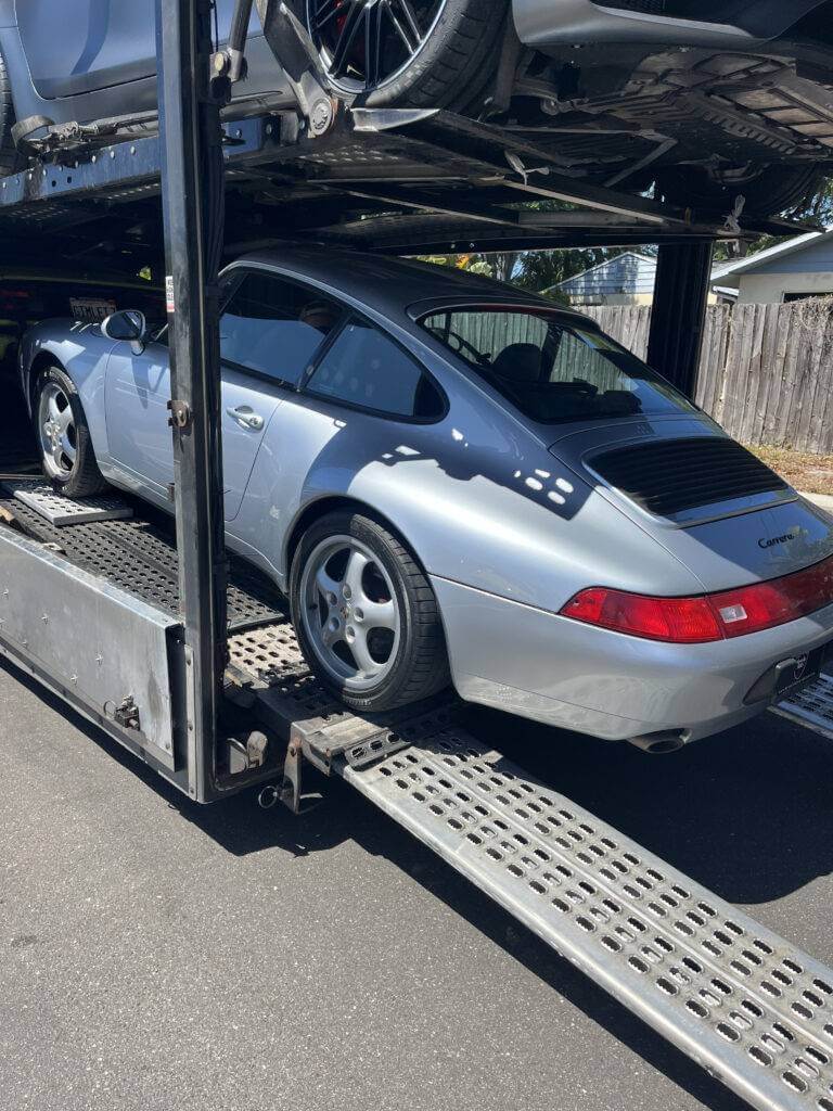A grey 1996 Porsche 993 loading on an open car transport trailer.