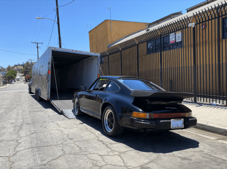 A 1980s Porsche 911 loading into a two-car covered trailer.